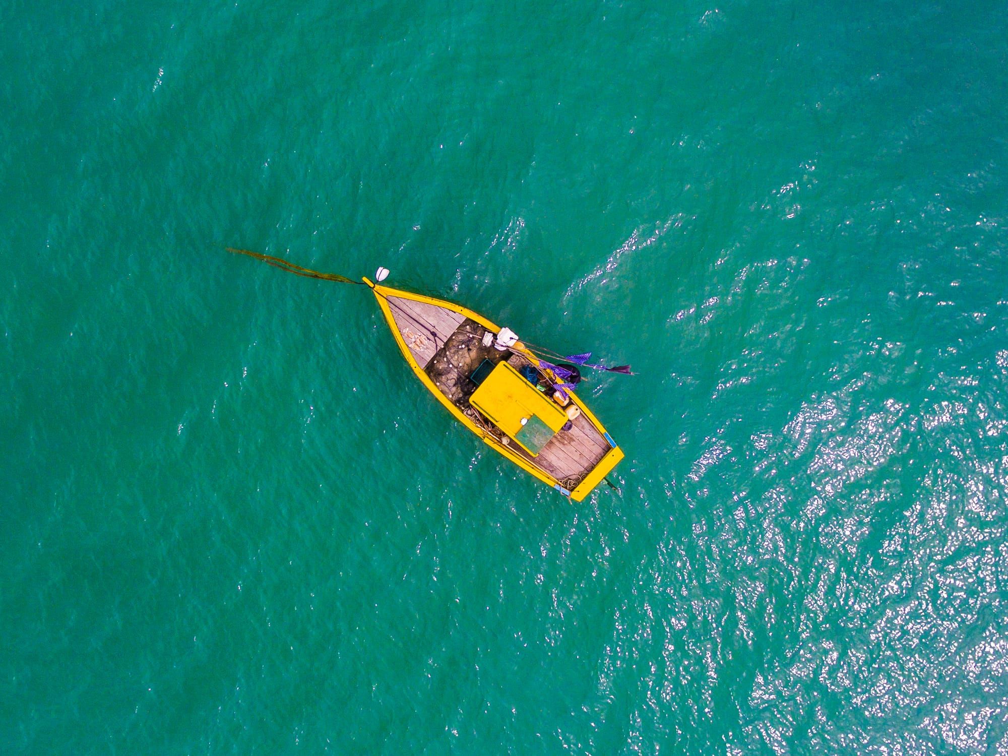 Barco de pesca amarelo visto de cima sobre o mar verde-esmeralda de Curuípe