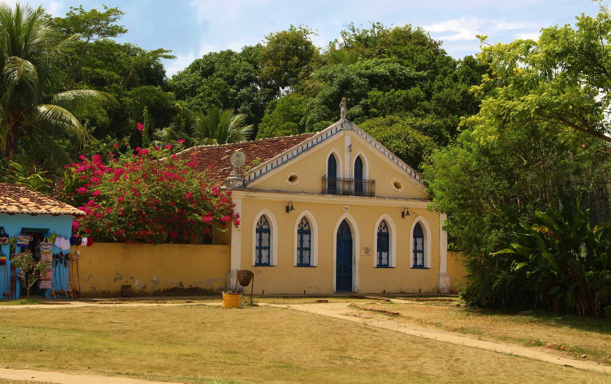 Igreja de fachada amarela e branca na Cidade Histórica de Porto Seguro, cercada de árvores floridas
