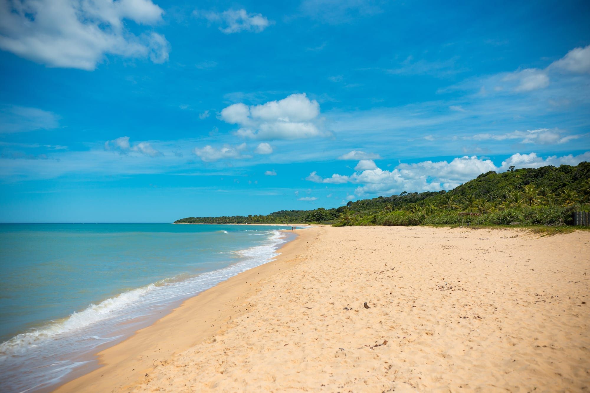 Praia de Itapororoca, ao sul de Trancoso, com faixa larga de areia, mar azul e falésia coberta de mata